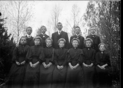 Gruppebilde 1900 - 05  Ytre Enebakk
Konfirmasjonsbilde 7 jenter, 5 gutter. Utendørs, svarte kjoler.
Nøkkelord: gruppebilde;konfirmasjon;ytre;gutter;jenter;kjoler;dress;pyntet;utendørs;trær;smykker
