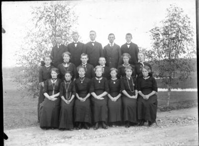 Gruppebilde 1900 -10  Ytre Enebakk
Konfirmasjonsbilde 11 jenter, 7 gutter. Utendørs, svarte kjoler
Nøkkelord: gruppebilde;konfirmasjon;ytre;gutter;jenter;kjoler;dress;pyntet;utendørs;tre;smykker