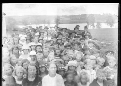 Gruppebilde  1910 - 20
Gruppe barn og voksne samlet i skolegården ved Ytre Enebakk skole. Pyntet - kanskje 17. Mai? 
Nøkkelord: gruppe;barn;voksne;ytre;skole