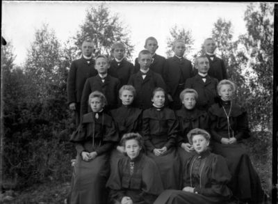 Gruppebilde 1900 - 05  Ytre Enebakk
Konfirmasjonsbilde 7 jenter, 8 gutter. Utendørs, svarte kjoler.
Nøkkelord: gruppebilde;konfirmasjon;ytre;gutter;jenter;kjole;dress;smykker;trær;utendørs;pyntet